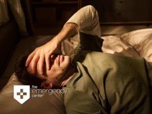 A man lies awake in bed at night with his hand over his face, showing signs of distress